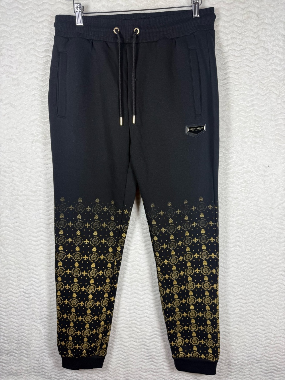 Supply & Demand Royalty MonoJogger Pants featuring a black and gold fleur-de-lis